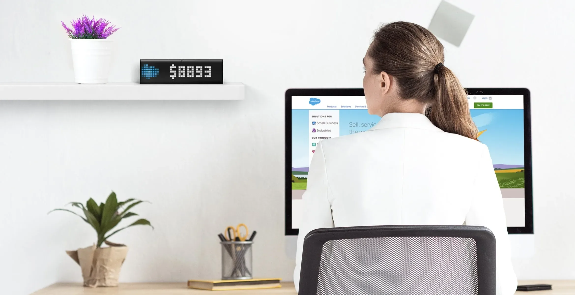 Saleswomen, working on the computer and looking on LaMetric Time smart clock, which displays revenue from the SalesForce